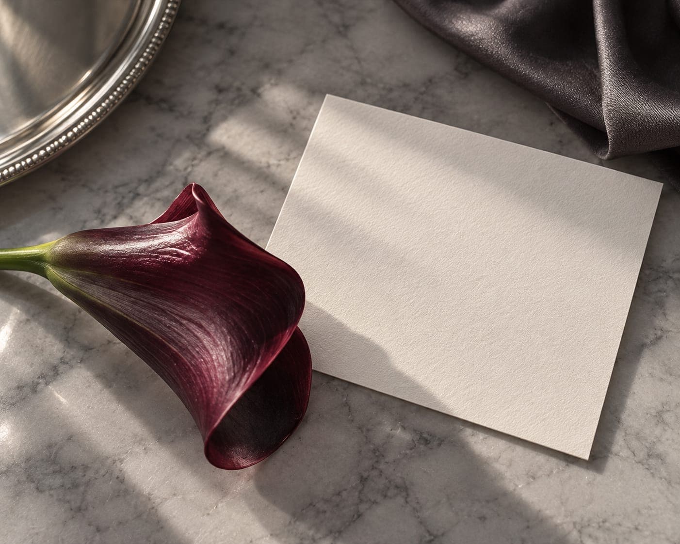 A burgundy calla lily beside a blank ivory card and a silver tray